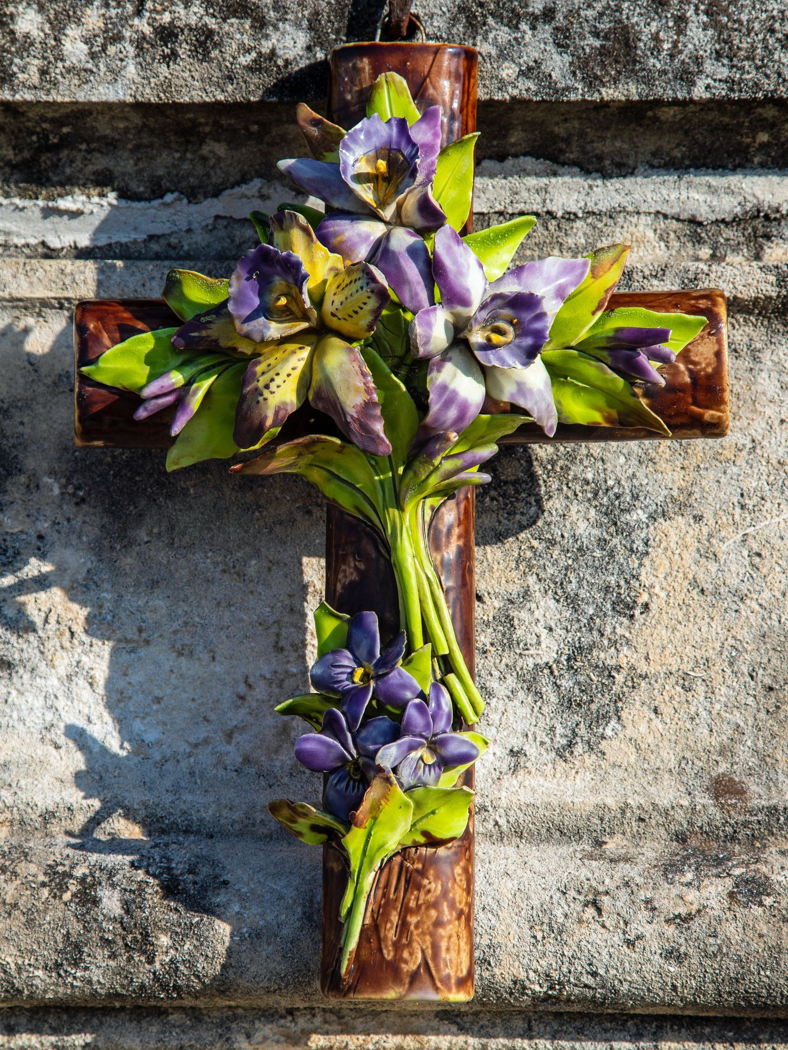 Des fleurs violettes disposées sur une croix en bois contre un mur de pierre