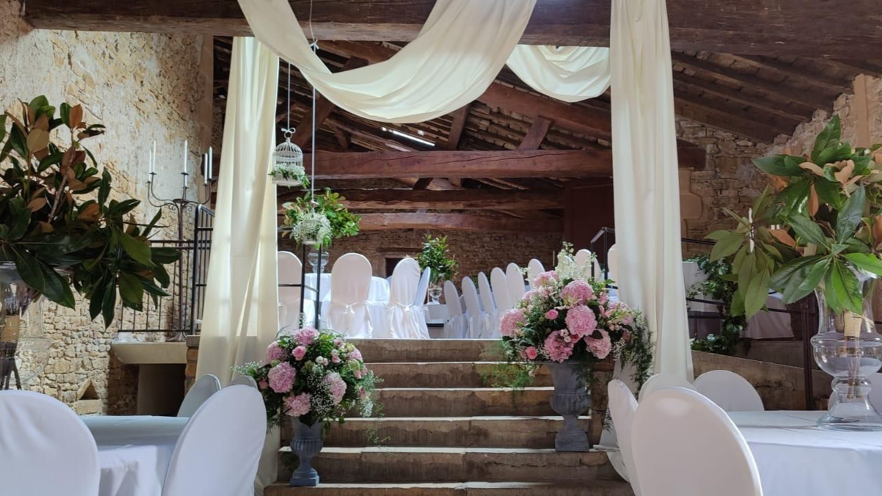 Scène de mariage élégante avec des draperies blanches, des compositions florales et des marches en pierre dans un lieu rustique