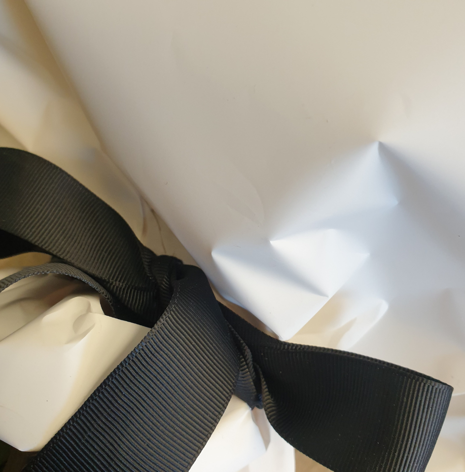 Sac cadeau blanc avec un nœud en ruban noir autour.