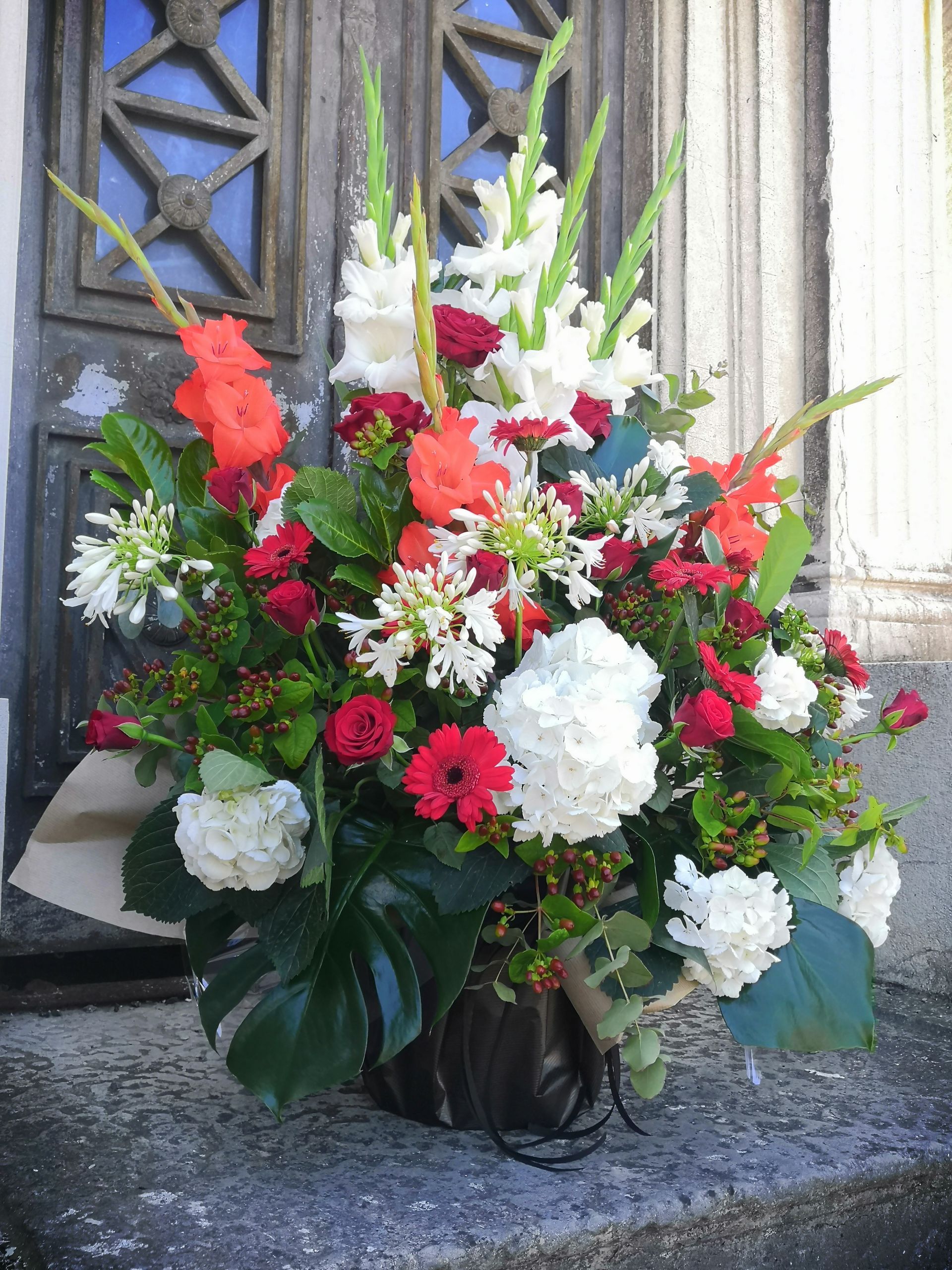 Composition florale colorée avec des fleurs rouges, blanches et vertes devant une porte en pierre