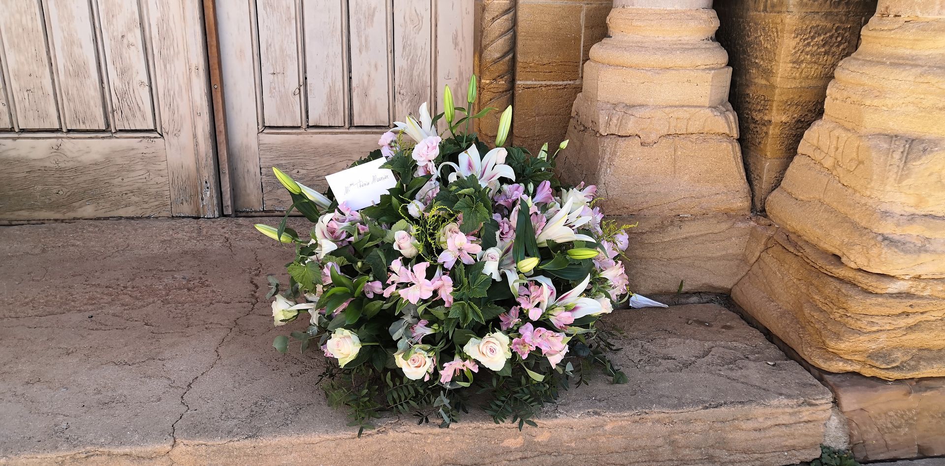 Bouquet de fleurs blanches et roses déposé sur un seuil en pierre près d'une porte en bois