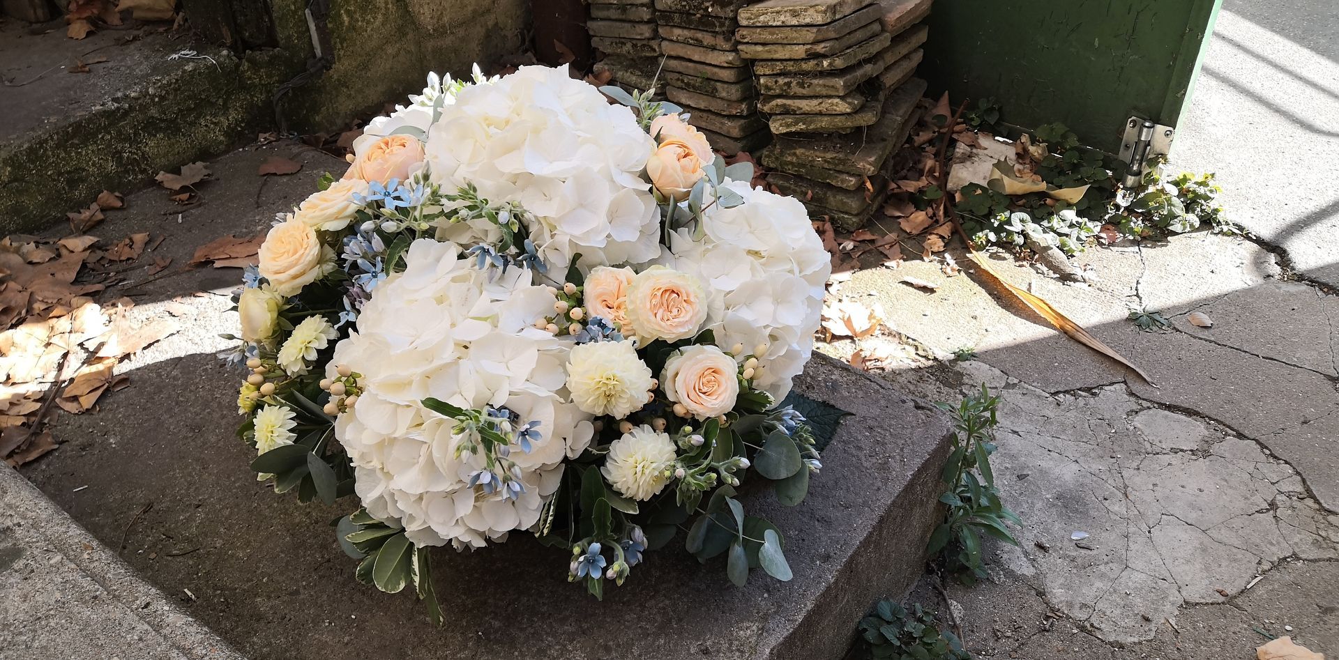 Bouquet de fleurs blanches et pêche sur un banc de pierre à l'extérieur, avec de la verdure et du soleil à proximité