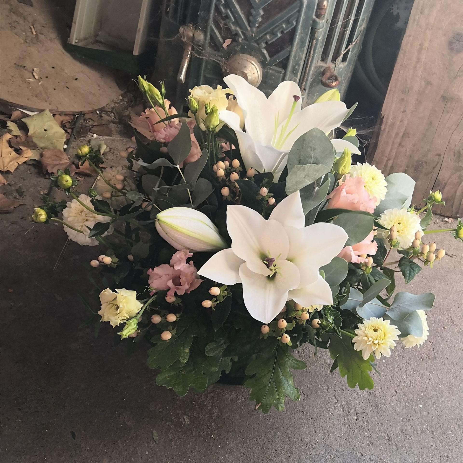 Des lys blancs et des fleurs pastel disposés en un petit bouquet floral sur le sol près d'une porte