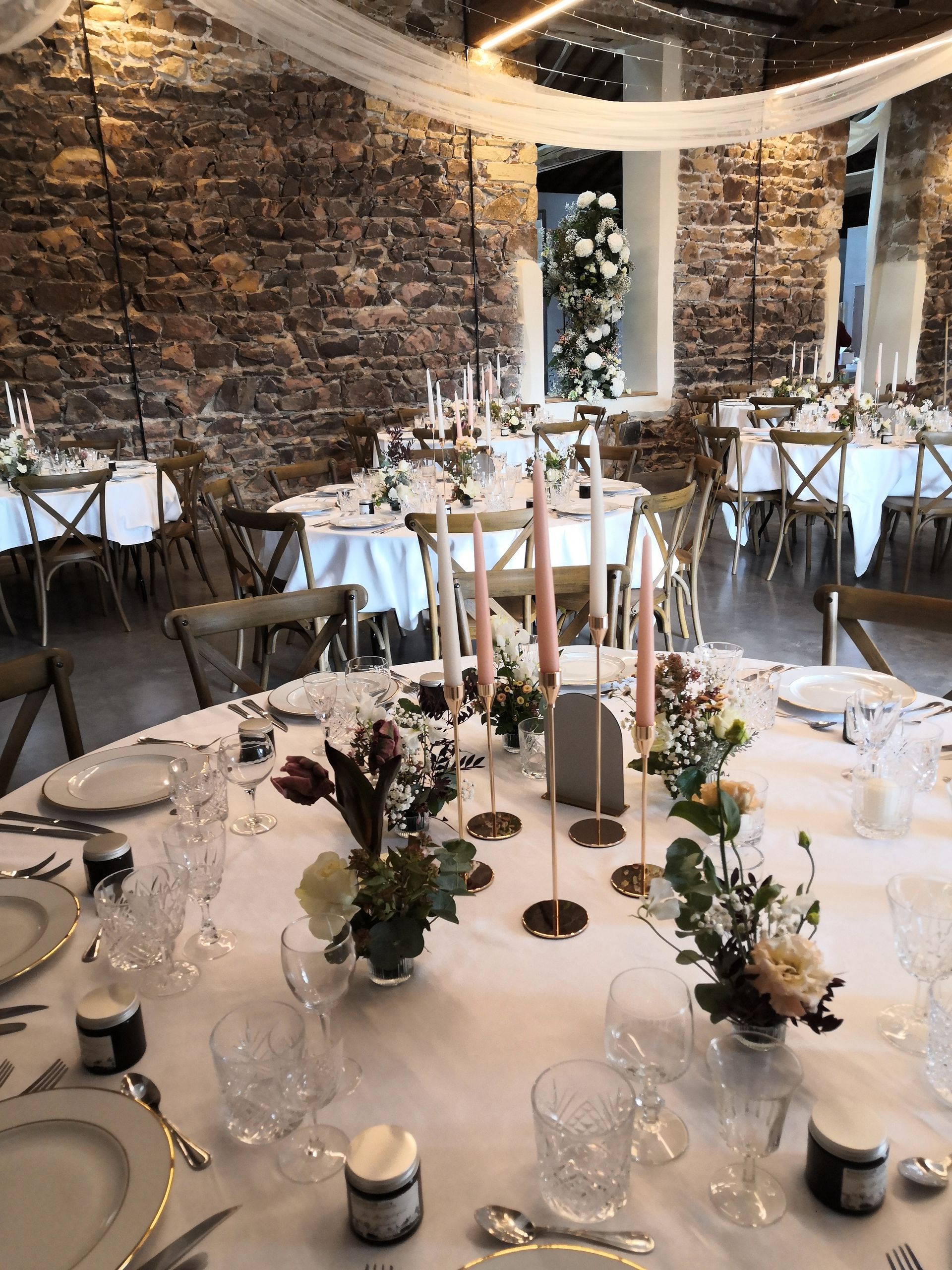 Élégante table de banquet avec nappes blanches, bougies et centres de table floraux dans une salle à manger rustique aux murs de pierre