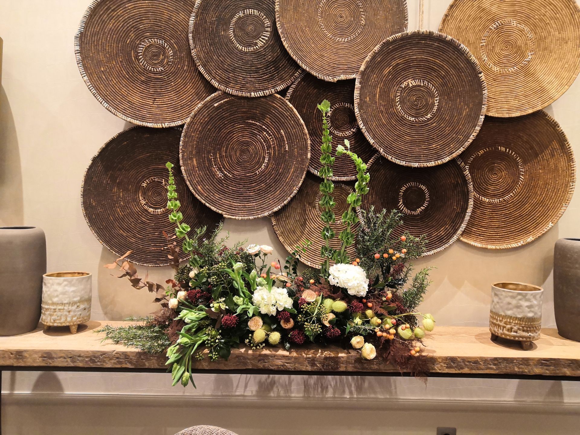 Centre de table floral décoratif avec cercles muraux tissés et bougies sur une table dans une pièce aux tons chauds