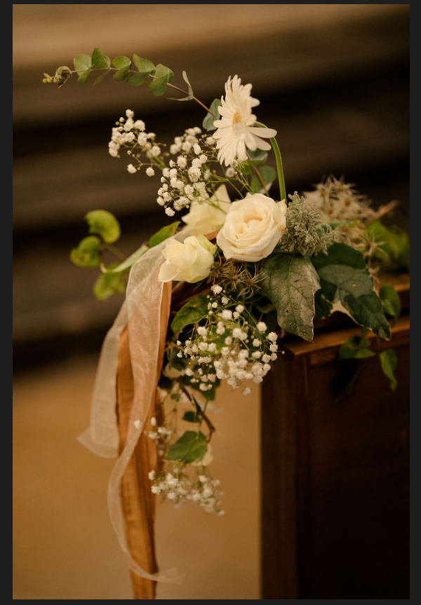 Composition florale blanche avec roses et feuillage sur un support en bois, agrémentée d'un ruban beige