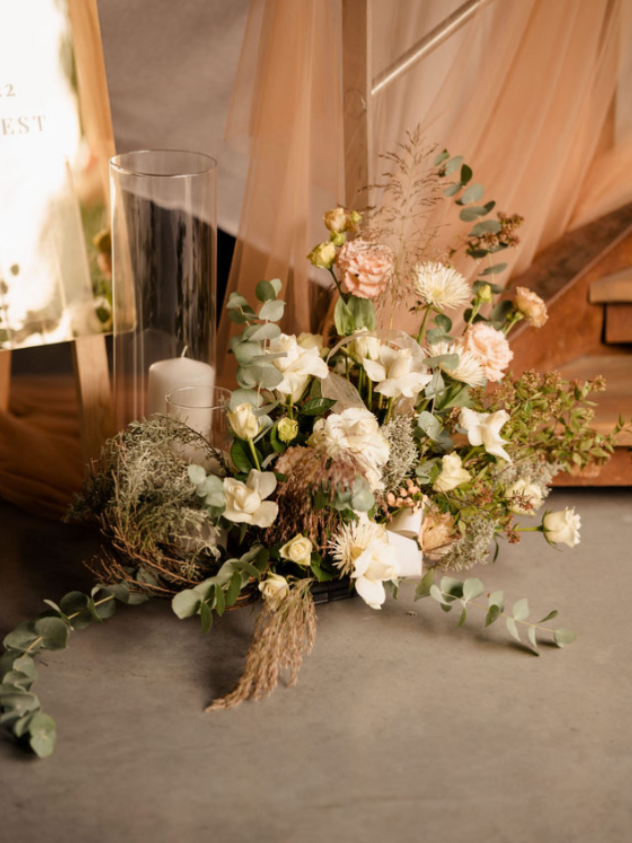 Élégante composition florale blanche et rose poudré avec de la verdure, disposée à l'intérieur à côté de voilages et d'un miroir.