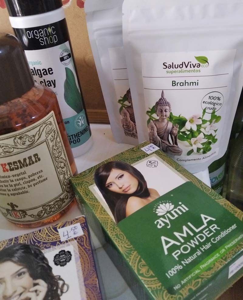 Una caja de polvo de amla está sobre una mesa junto a otros productos para el cabello.