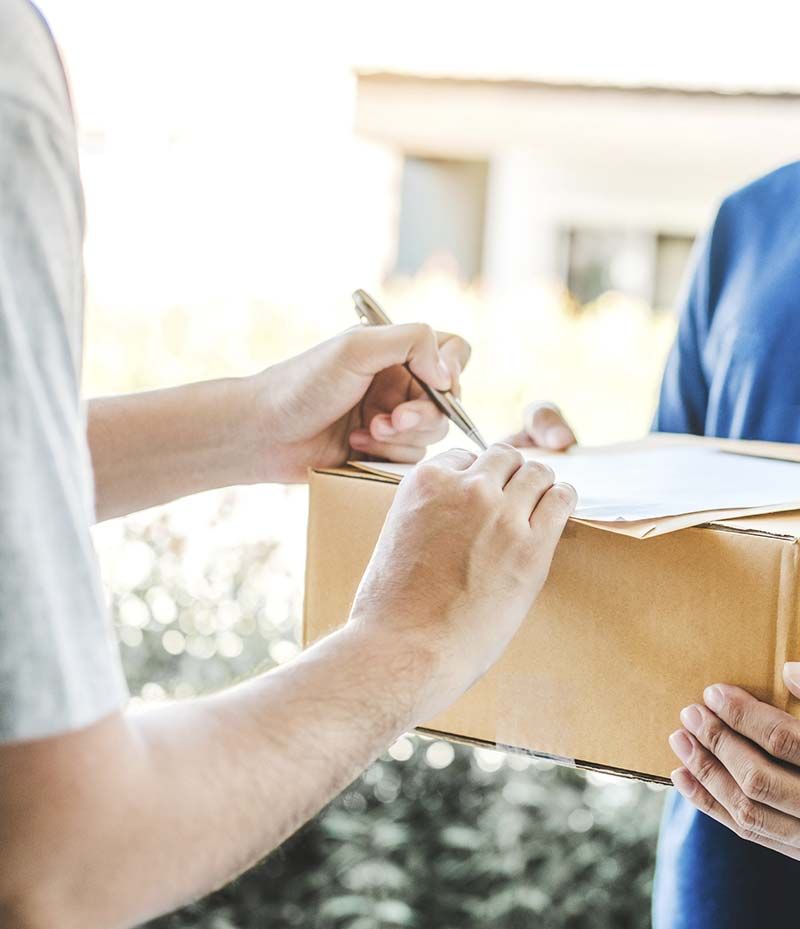 Un hombre está firmando un trozo de papel mientras sostiene una caja de cartón.