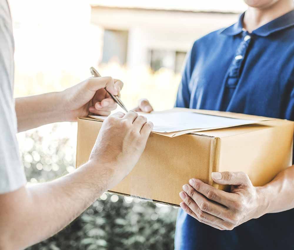 Un hombre sostiene una caja de cartón y firma un trozo de papel.