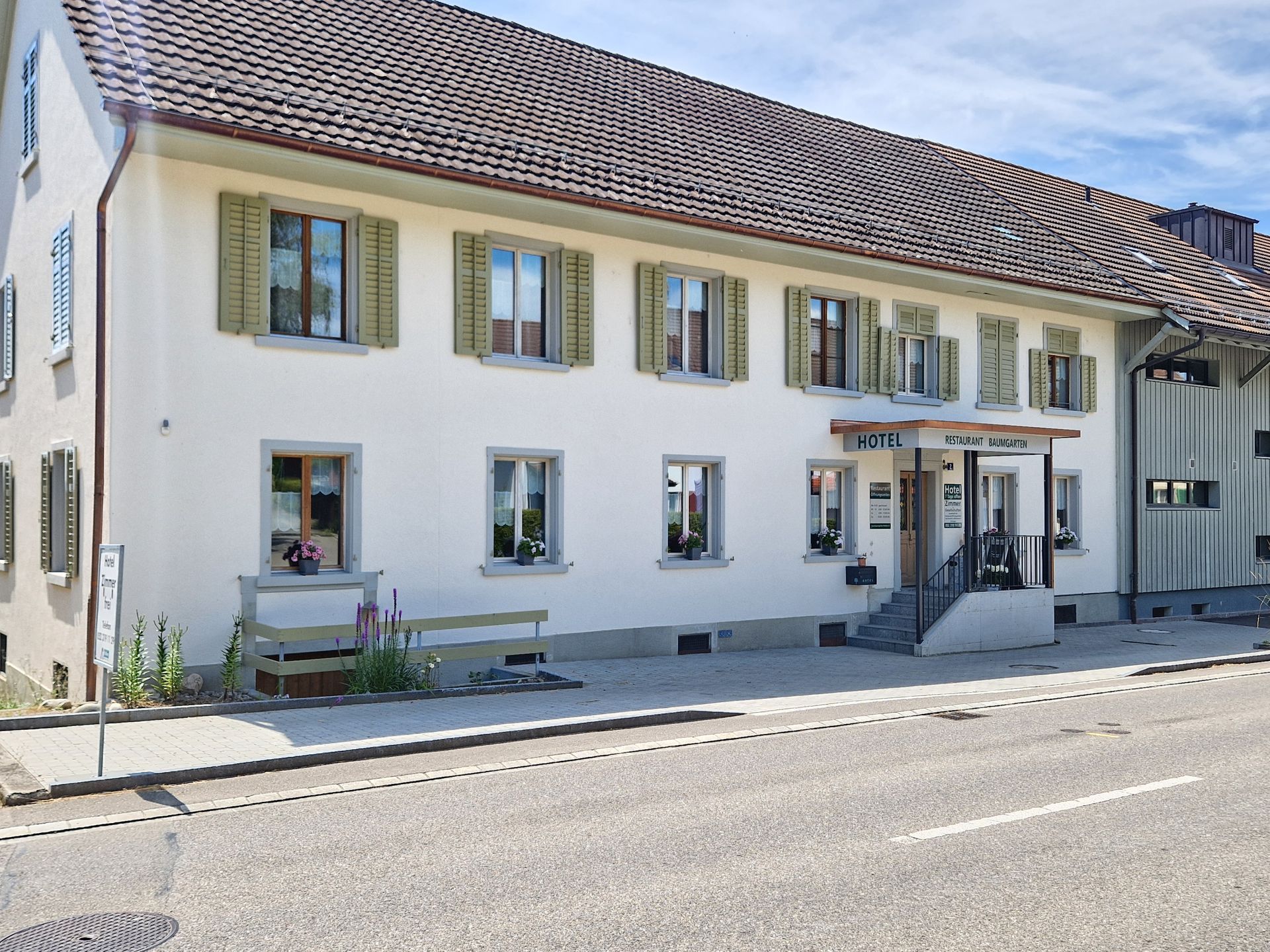 Am Straßenrand steht ein großes weißes Gebäude mit einem braunen Dach.
