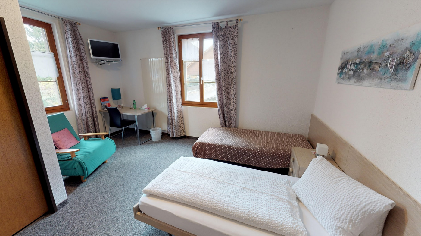 Ein Schlafzimmer mit zwei Betten, einem Stuhl, einem Schreibtisch und einem Fernseher.