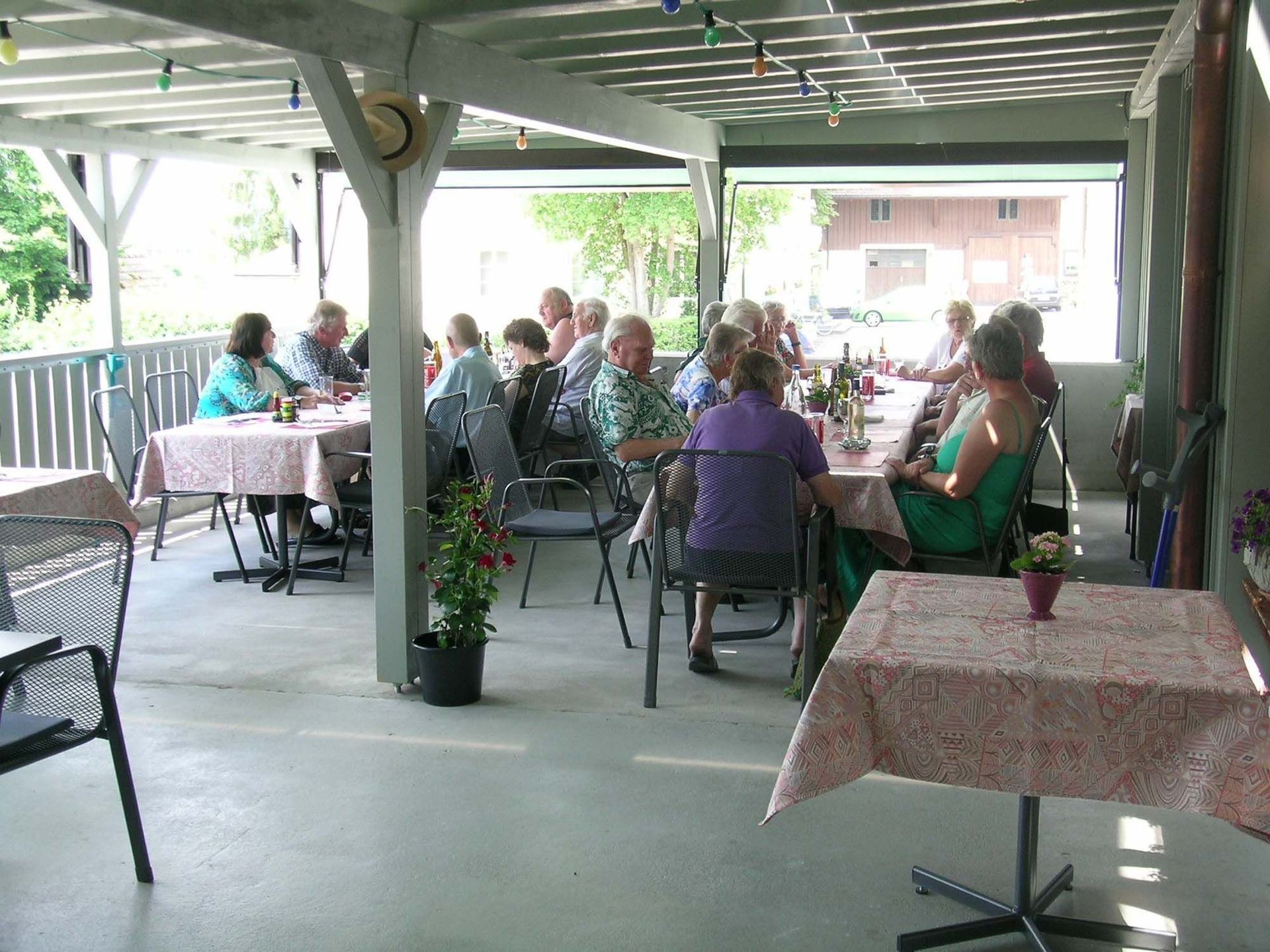 Eine Gruppe von Leuten sitzt an Tischen unter einer überdachten Veranda.
