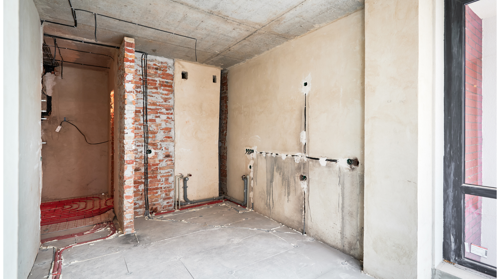 Intérieur d'une pièce en construction, avec briques apparentes, murs en béton et câblage non terminé.