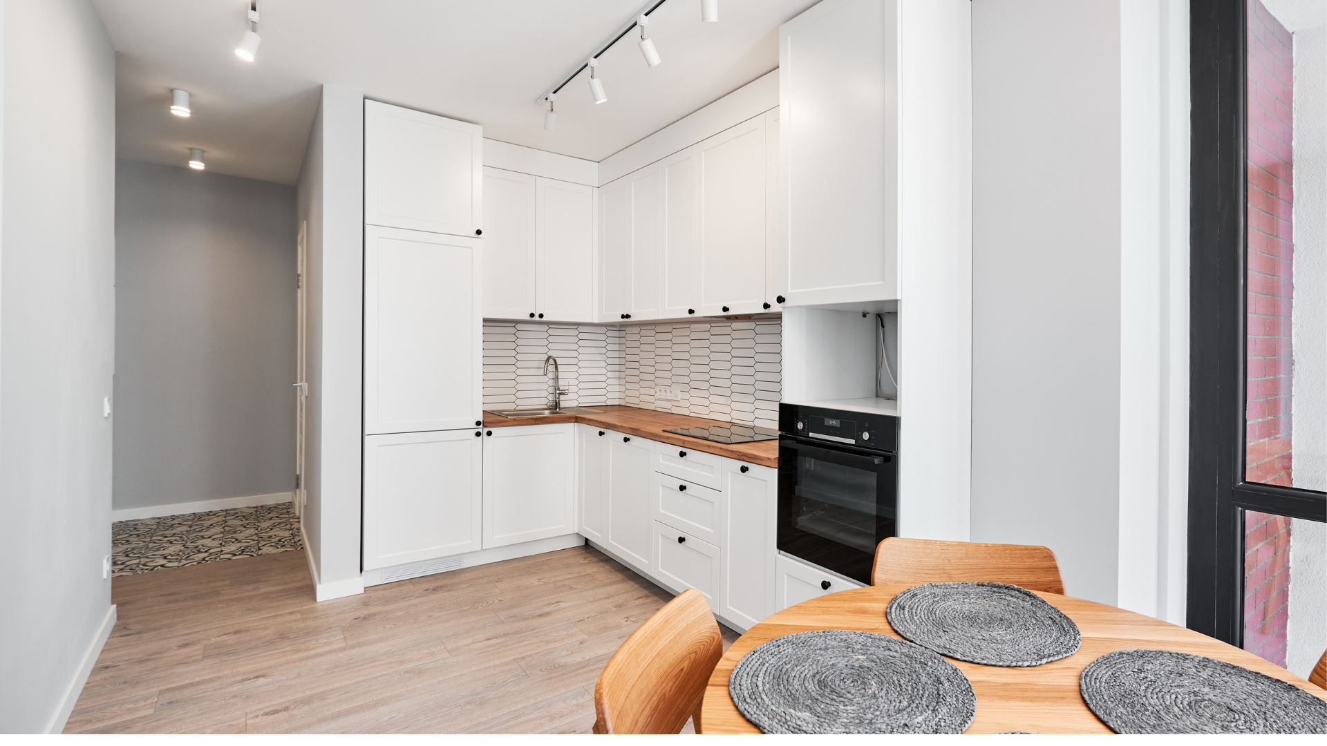 Cuisine blanche avec plans de travail et four en bois, parquet clair et table à manger avec chaises.