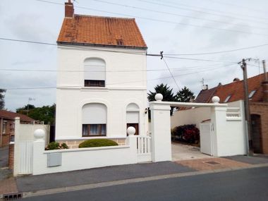 Maison blanche avec toit de tuiles rouges, clôture blanche et allée privée dans une rue résidentielle.