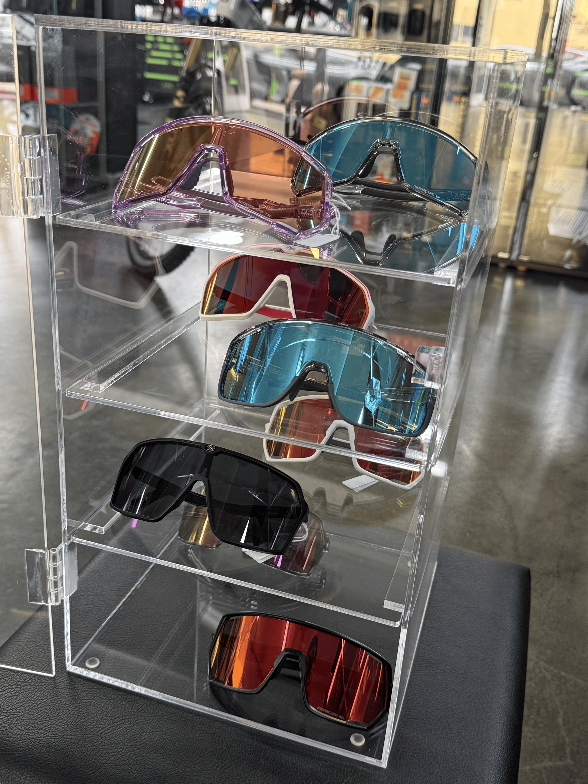 Gafas de sol expuestas en un soporte transparente en una tienda, con lentes espejadas en rosa, azul, negro y rojo.