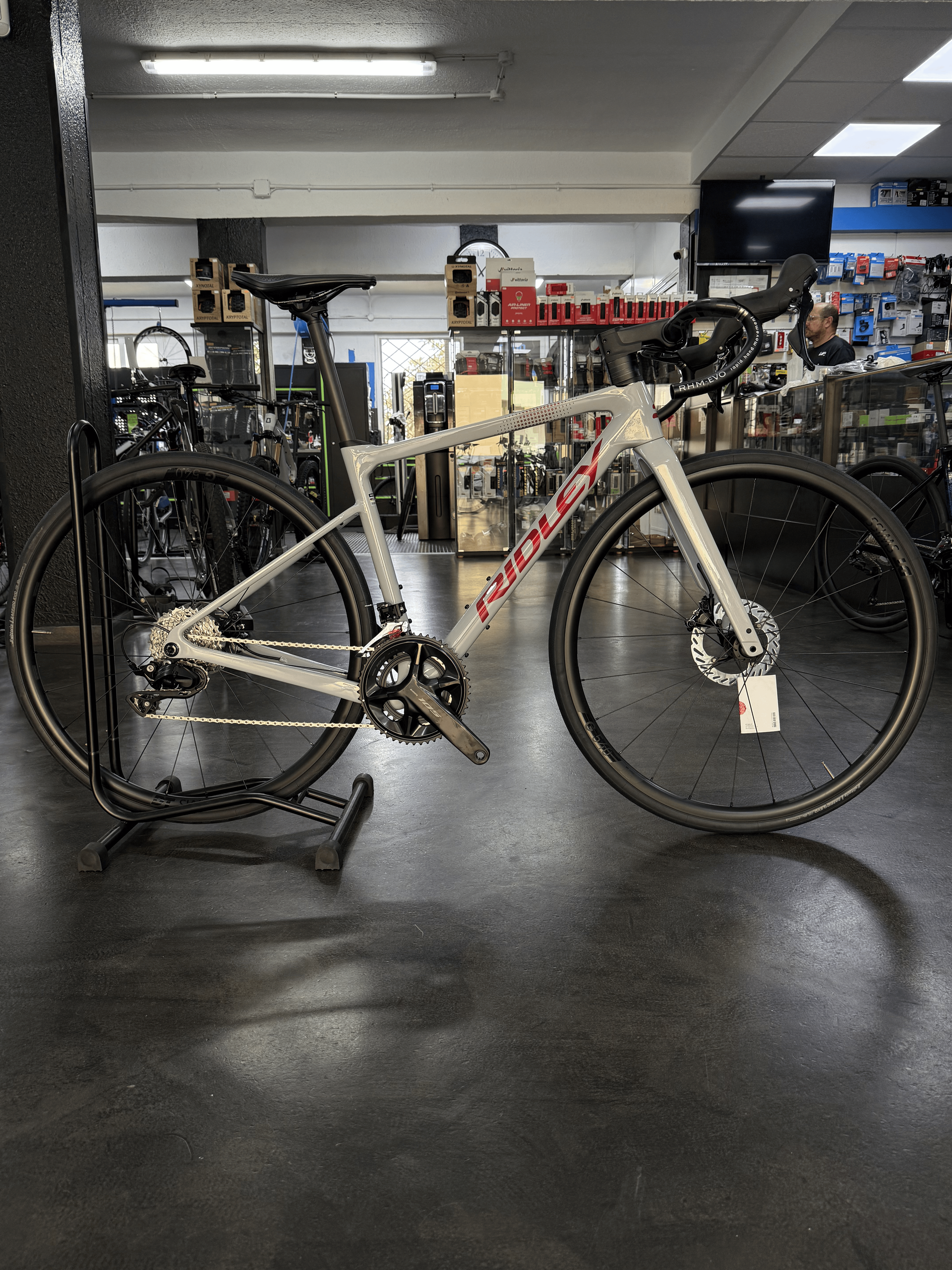 Bicicleta de montaña color canela expuesta en el interior de una tienda de bicicletas, con ruedas negras y suelo gris.