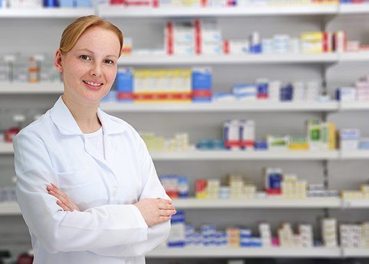 Una farmacéutica está de pie en una farmacia con los brazos cruzados.