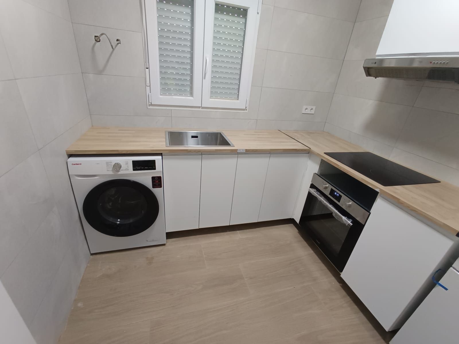 Pequeña cocina moderna con gabinetes blancos, encimeras de madera clara y lavadora.