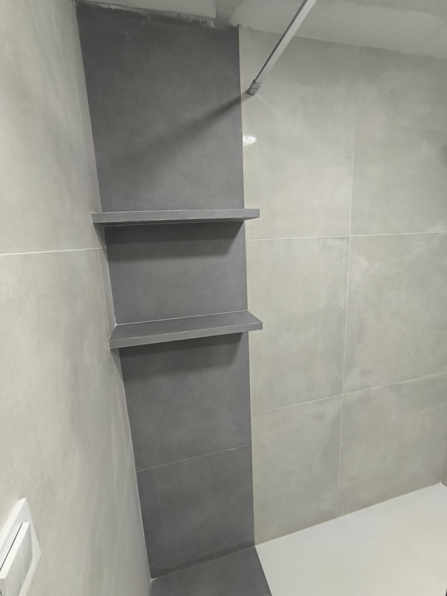 Ducha con azulejos grises y estantes incorporados.