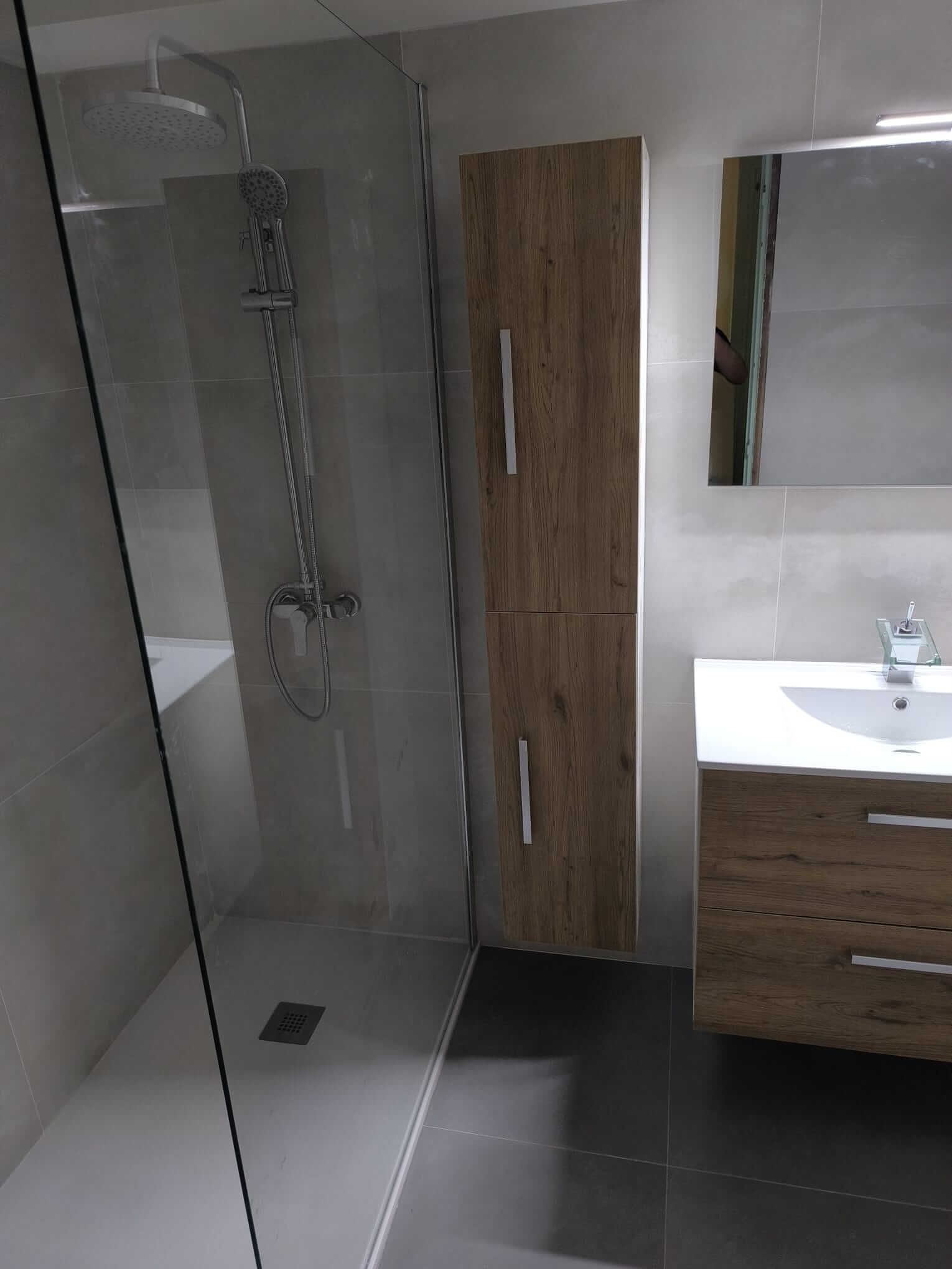 Baño moderno con ducha, mueble de almacenaje con vetas de madera y tocador.