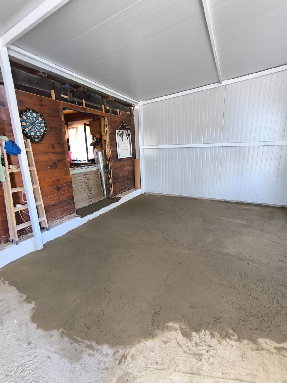 Habitación recién cementada con paredes de madera, tablero de dardos y escalera.