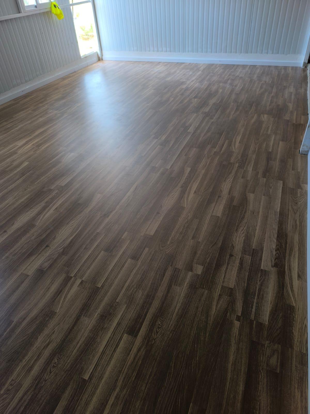 Piso de madera de color marrón oscuro en una habitación vacía con revestimiento de madera blanco.