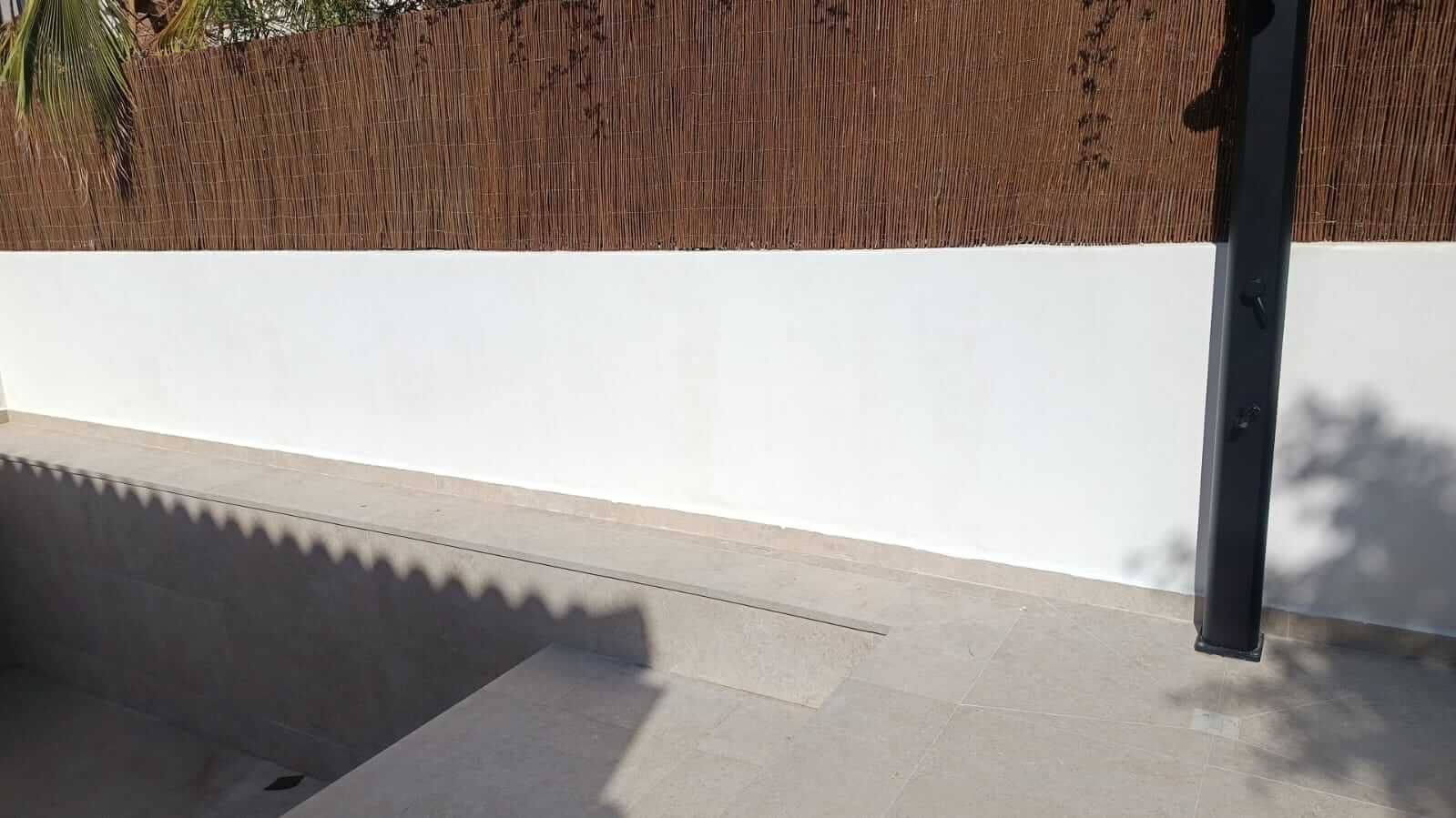 Pared blanca con techo de paja marrón encima, escalones y suelo de piedra gris.