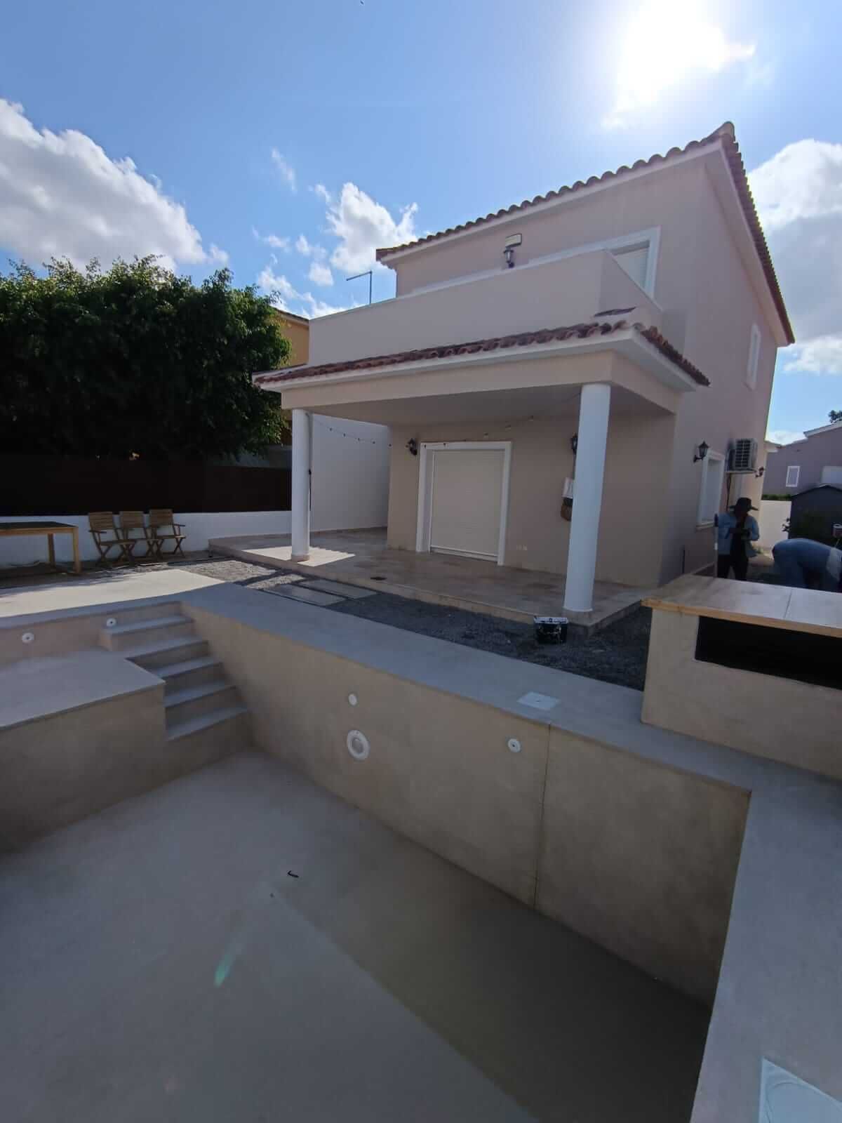 Una casa beige de dos pisos con piscina en construcción en un día soleado.