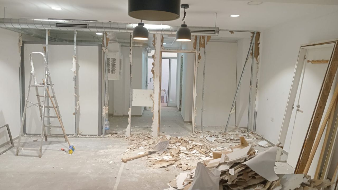Reforma interior en curso: escombros en suelo, paredes parcialmente demolidas con puertas y estructura expuesta, luces en el techo.