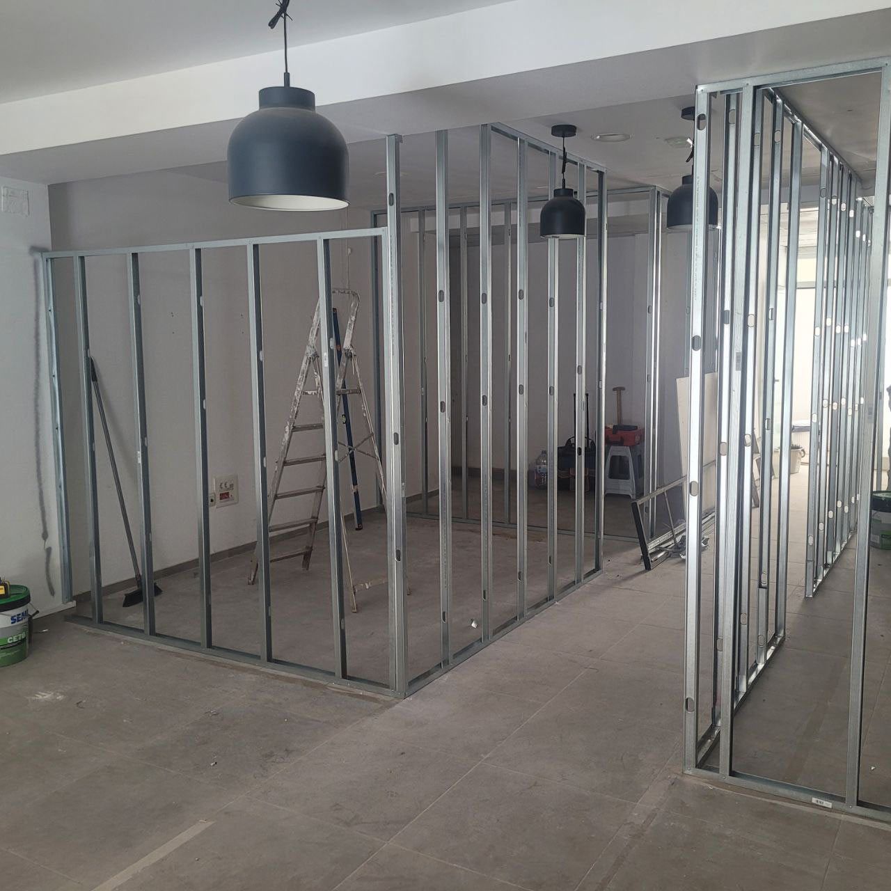 Los montantes metálicos forman las paredes de una habitación en construcción; dos lámparas colgantes cuelgan del techo.