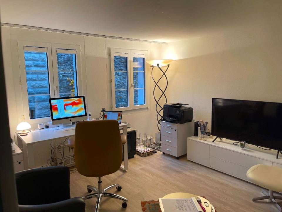 Heimbüro mit Schreibtisch, Computer und Fernseher. Natürliches Licht durch Fenster.