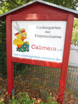 Ein rot umrahmtes Schild für den Kindergarten der Elterninitiative Calimero e.V. mit einer Comic-Ente in einer Gartenkulisse.