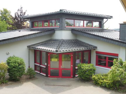 Ein niedriges, weißes Gebäude mit roten Fensterrahmen und Türen, das einen zentralen, erhöhten Dachabschnitt aufweist.