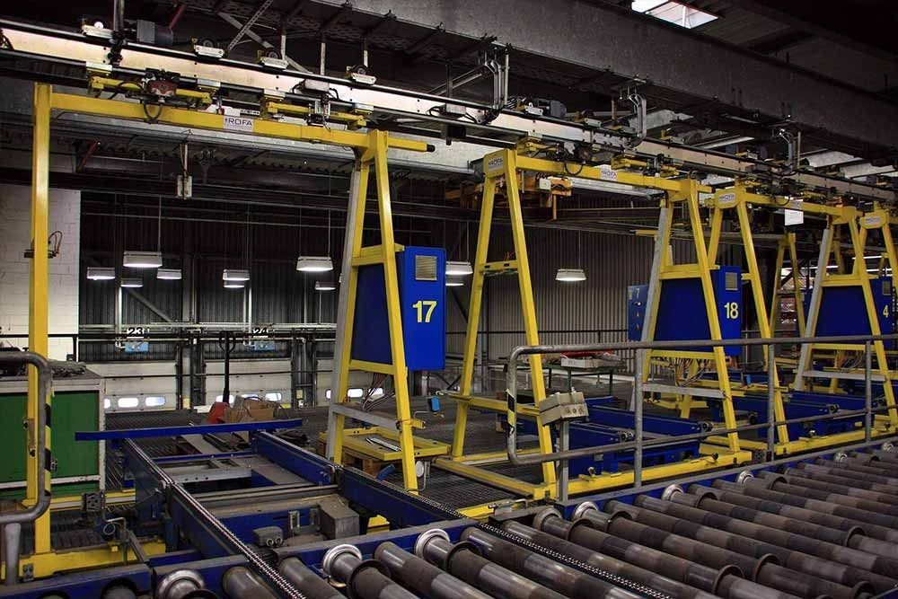 Maquinaria amarilla con componentes azules sobre un transportador de rodillos en un entorno industrial.