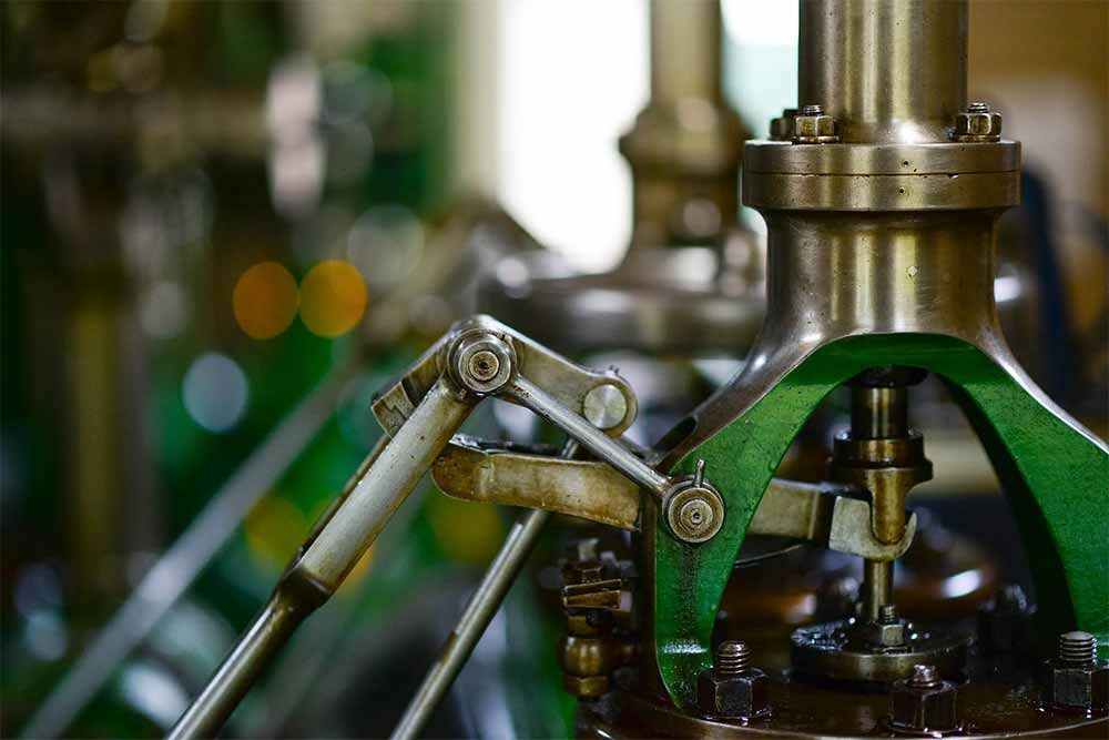 Primer plano de un mecanismo de motor de vapor verde y plateado con pernos, palancas y tubos.
