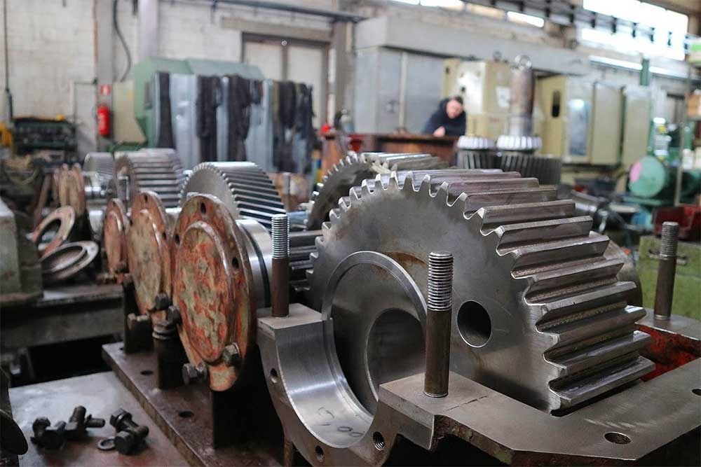 Engranajes y maquinaria en un taller industrial, con un trabajador al fondo.