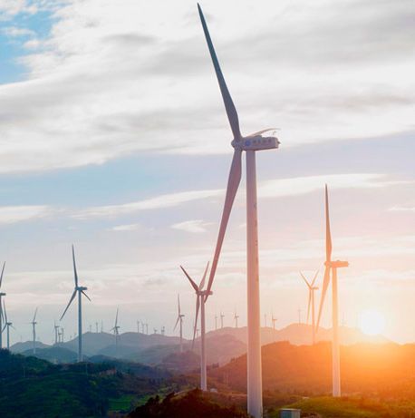 Una hilera de turbinas eólicas se encuentran en la cima de una colina al atardecer.