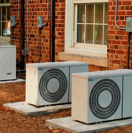 Dos aparatos de aire acondicionado están fuera de un edificio de ladrillos.