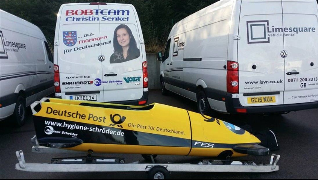 Sprinter mit einem Anhänger, auf welchem ein Bob von der Deutschen Post ist.