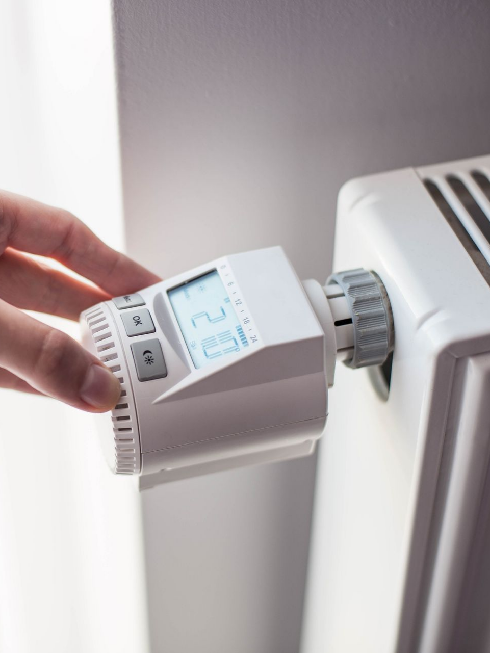Réglage manuel d'un thermostat numérique blanc sur un radiateur blanc.