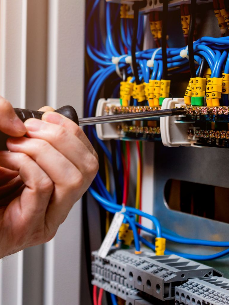 Une personne utilise un tournevis pour travailler sur le câblage électrique à l'intérieur d'un panneau de commande.