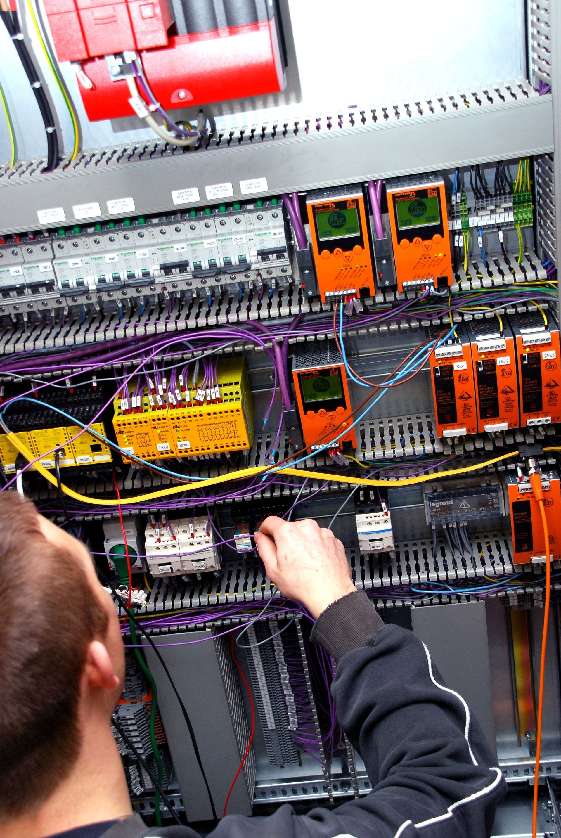 Personne travaillant sur un panneau de commande électrique complexe avec des fils et des composants colorés.