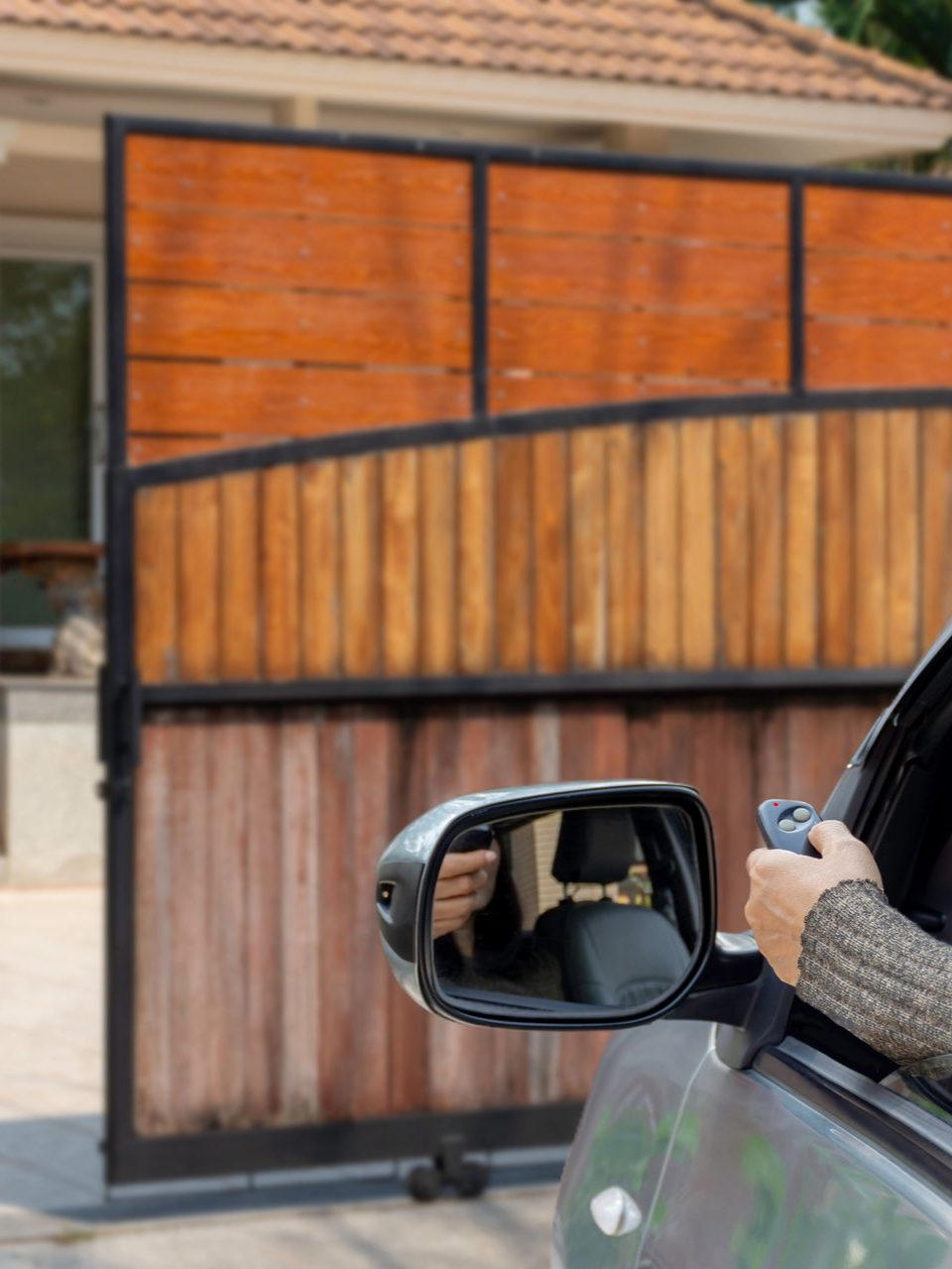 Une personne dans une voiture utilise une télécommande pour ouvrir un portail en bois.