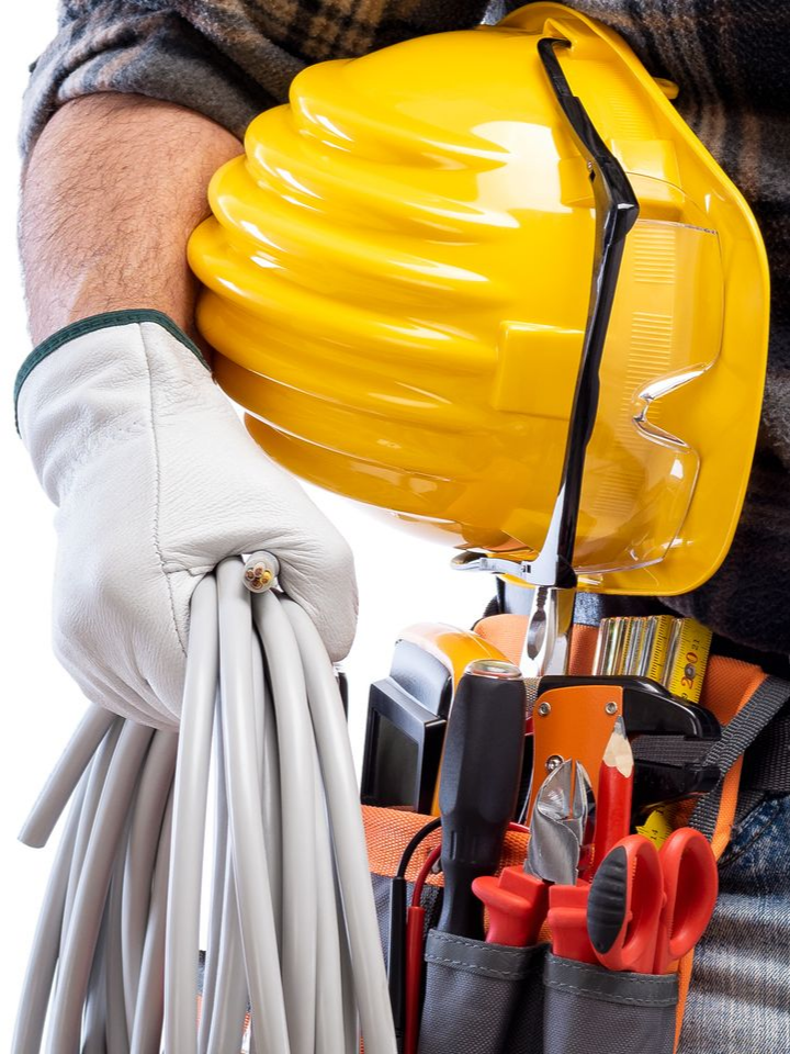 Personne portant des gants de travail, tenant un câble enroulé, un casque de chantier et une ceinture porte-outils.