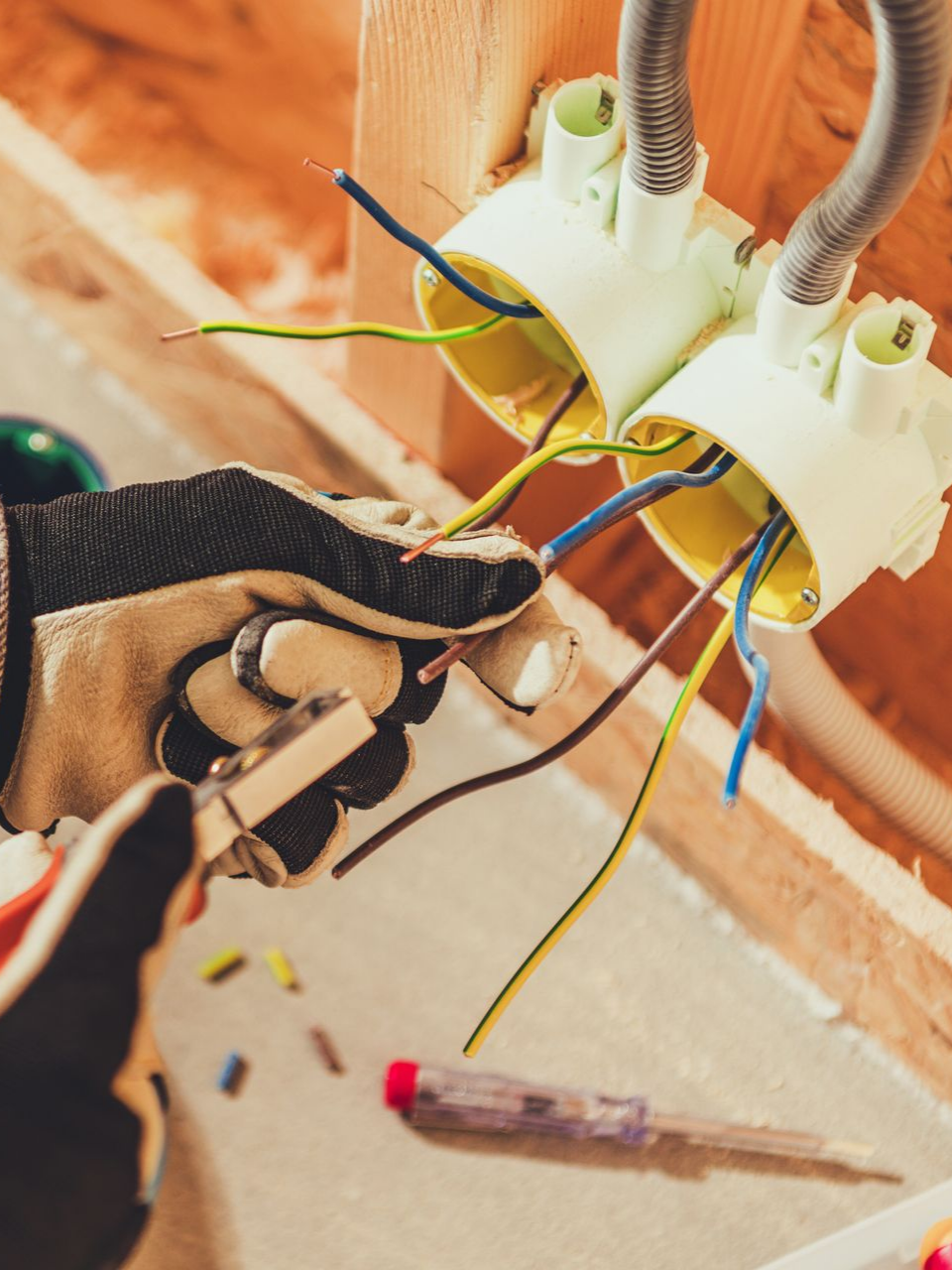 Électricien effectuant le câblage de boîtes de jonction électriques, portant des gants ; chantier de construction.