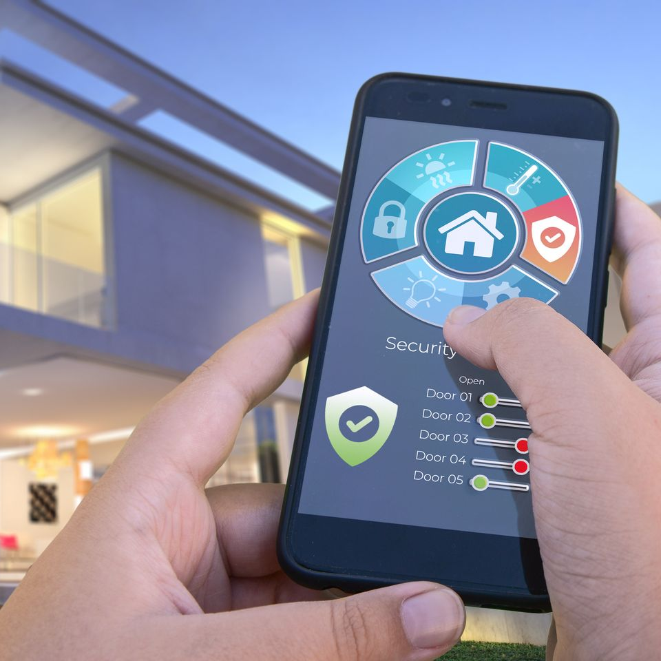 Personne utilisant un smartphone avec une application de sécurité domestique, surveillant la maison.