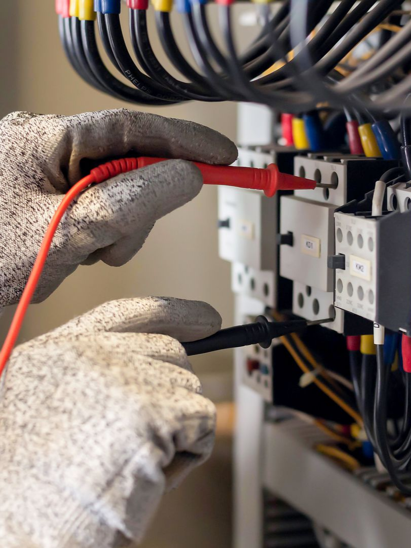 Électricien portant des gants testant un tableau électrique avec un multimètre.