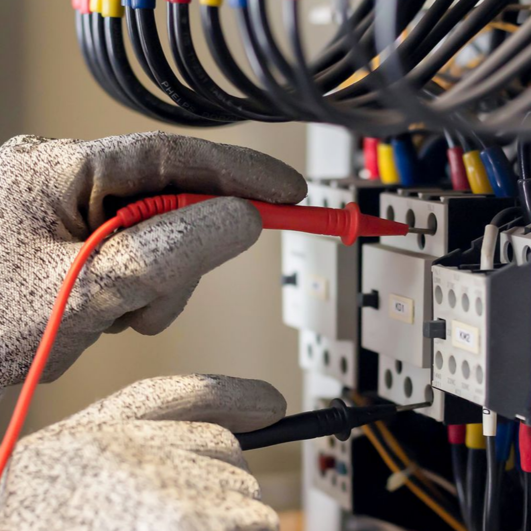 Mains gantées de gants de travail testant le câblage électrique avec un multimètre.